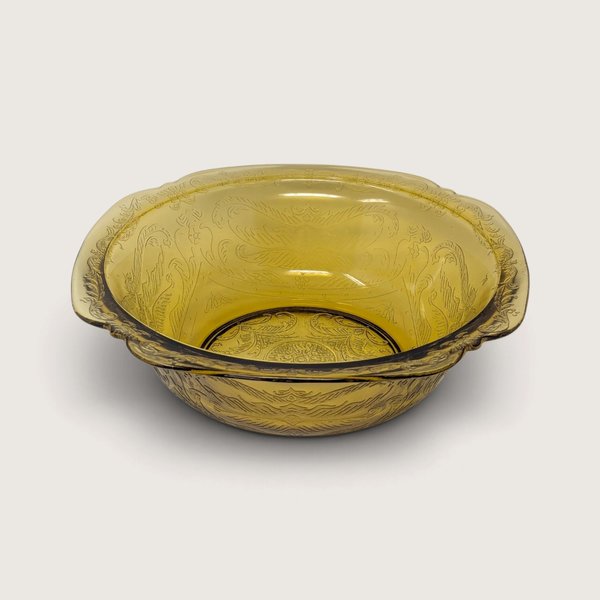 A vintage yellow glass serving bowl featuring an embossed scroll pattern on a neutral background.