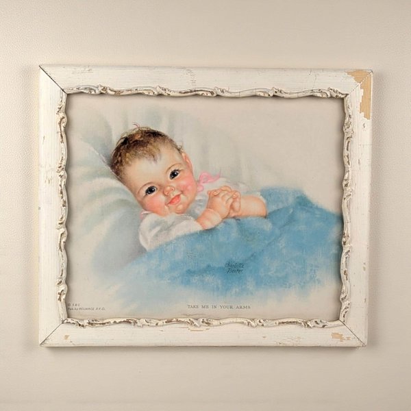 A horizontal vintage lithograph titled Take Me In Your Arms by Charlotte Becker. It depicts a rosy-cheeked baby with a pink bow under a blue blanket. The artwork is housed in a weathered white wood frame with carved scalloped inner detailing.
