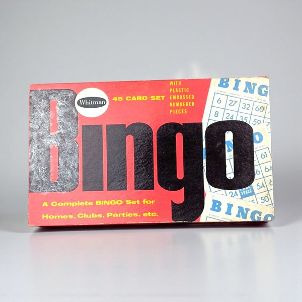 A rectangular vintage game box with a vibrant red background. Large black and gray "BINGO" text dominates the center, flanked by illustrations of blue and white bingo cards. The surface shows a slight linen-like texture and minor edge wear.