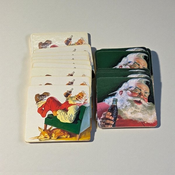 A collection of square cardboard coasters with rounded corners. Ten feature a seated Santa in a green armchair with a Coke bottle, and seven show a standing Santa holding a glass of Coca-Cola.