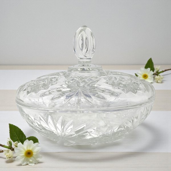 A clear glass serving dish with a matching lid featuring a starburst and pineapple pattern. The bowl has a scalloped rim and a pedestal-like base, while the lid is topped with a faceted pointed finial.