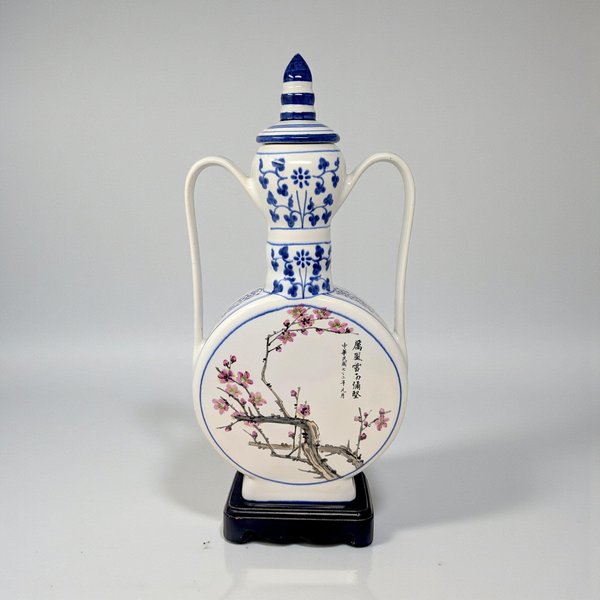 A large, circular porcelain moon flask with a slender neck and two small handles. The face features a detailed blue and white transfer of a blooming lotus and rose, set against a stark white glaze.