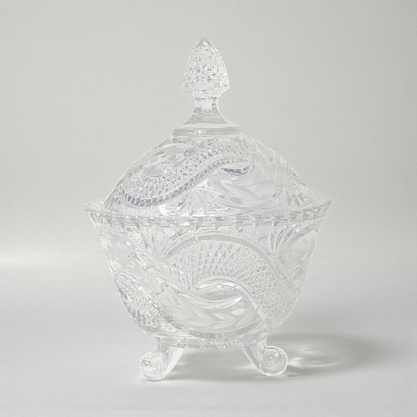 A tall, clear crystal candy dish with a matching lid. The exterior features a bold, swirling serpentine texture that winds around the body and finial, creating a fluid, rippled glass effect.