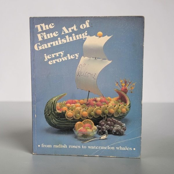 A softcover book featuring a vibrant blue cover with a large photograph of a watermelon carved into a sailing ship filled with fruit. The typography is a bold, creamy white sans-serif. The edges show light shelf wear consistent with its matte paper finish.