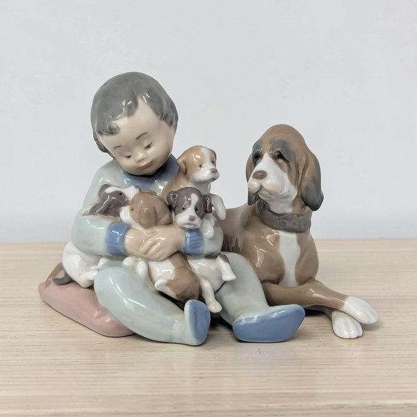 A pale blue and white glazed porcelain figurine featuring a young girl in a long dress kneeling beside a small puppy. The girl wears a wide-brimmed sun hat, and the piece is finished in the signature Lladro pastel color palette.