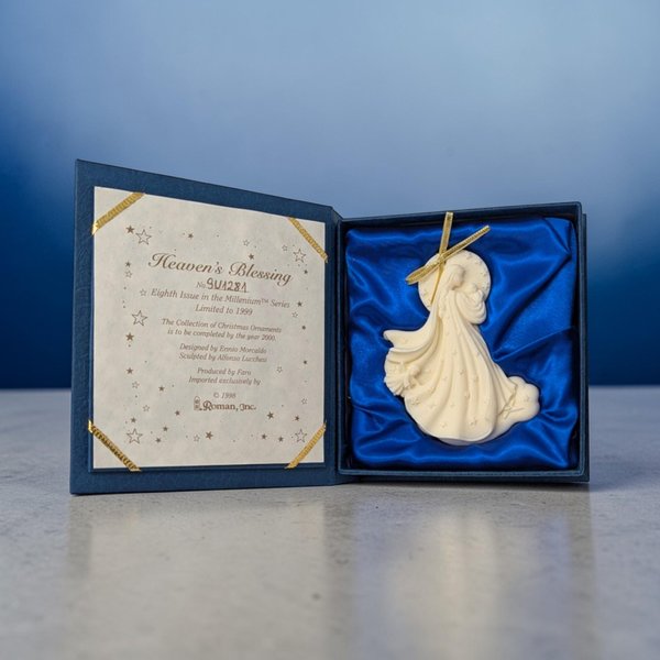A ceramic ornament featuring a relief carving of a winged angel holding a small child. The scene is finished in a monochromatic cream glaze with a gold-tone hanging cord attached to the top.