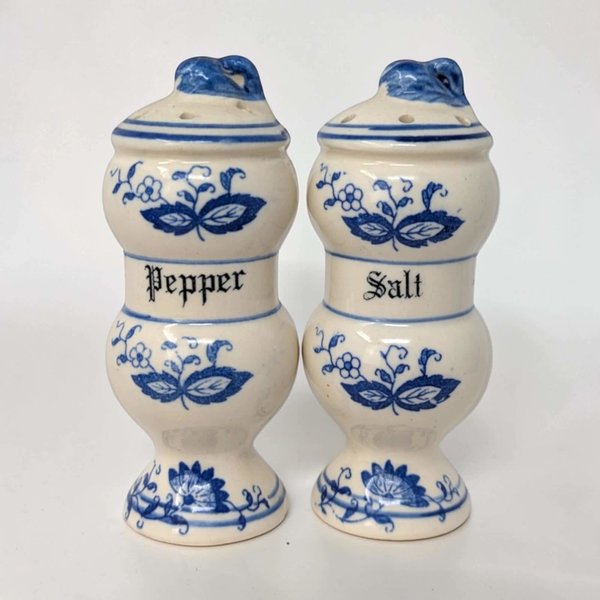 A pair of white ceramic salt and pepper shakers with a blue floral pattern. Each tall, rectangular shaker features a blue rim at the base and top, with traditional onion motifs on the front. They have plastic stoppers at the bottom.