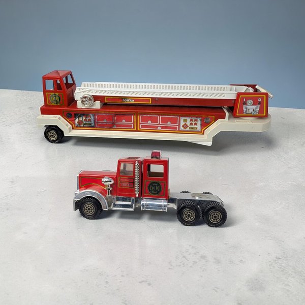 A 33-inch two-piece red Tonka fire truck with a long horizontal silhouette and a hard metal and plastic texture. It features a white extendable ladder, silver-tone cab accents, and small star-shaped sticker remnants on the body.