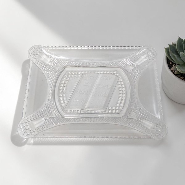 A rectangular clear pressed glass plate with a central embossed open Bible motif featuring the phrase Give Us This Day Our Daily Bread. The plate has a textured diamond-patterned border and raised, faceted corner handles.