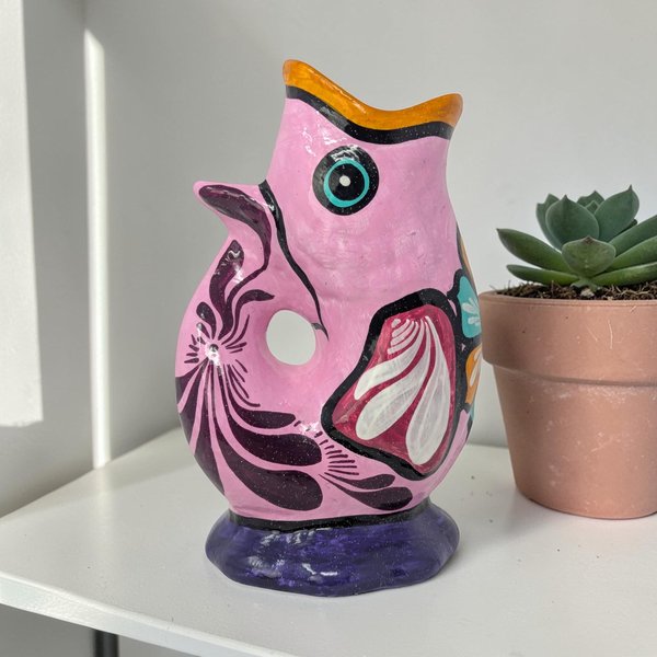A ceramic vase shaped like a fish with a rounded body and a flared mouth. The texture is a matte, earthy terracotta with hand-painted floral and scale details in blue and grey tones.