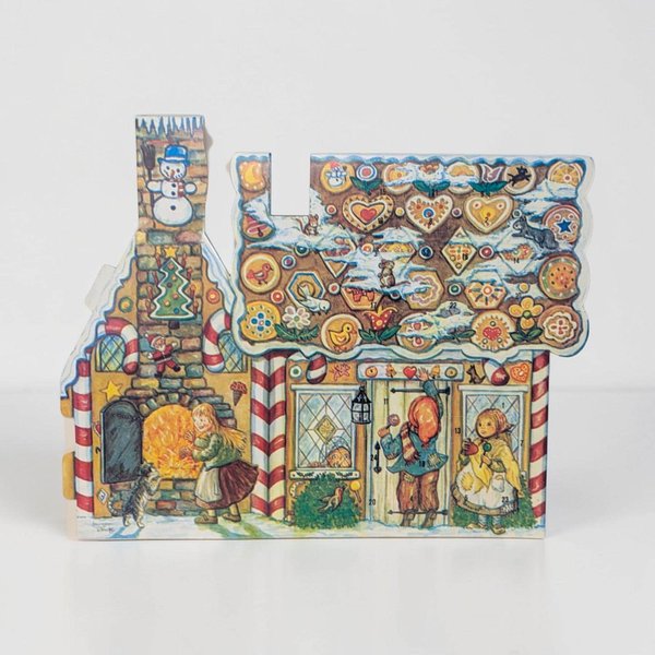 A colorful cardstock advent calendar shaped like a charming two-story cottage. The illustration features a snowy roof, festive wreaths on the windows, and a vibrant red door. The silhouette is die-cut following the peaked roofline and chimney.