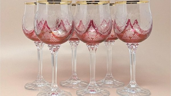A set of six wine glasses with cranberry red bowls featuring frosted etched floral patterns and gold rims. The stems are tall, clear, and multi-faceted with a flat circular base.